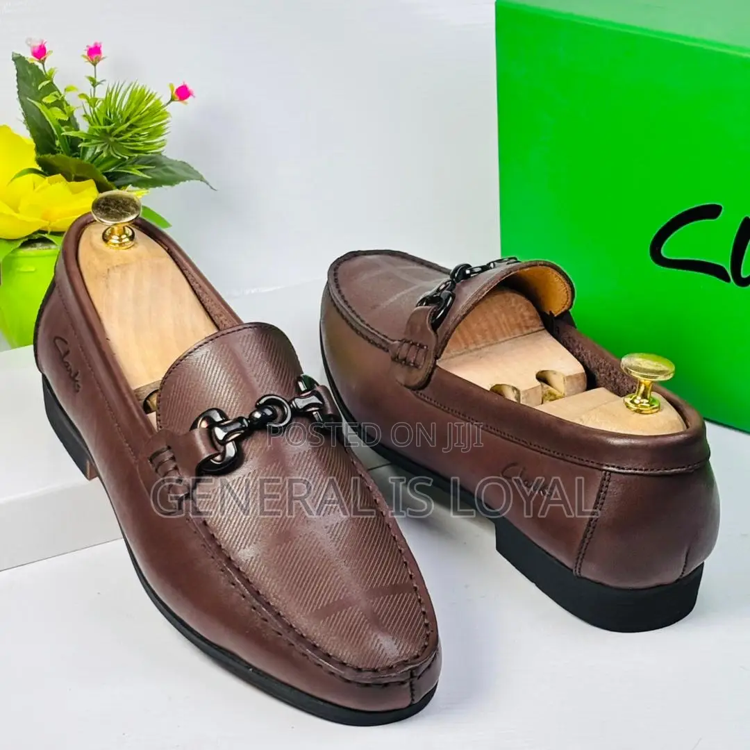 Brown Clarks Loafers With A Metal Buckle And Patterned Leather.