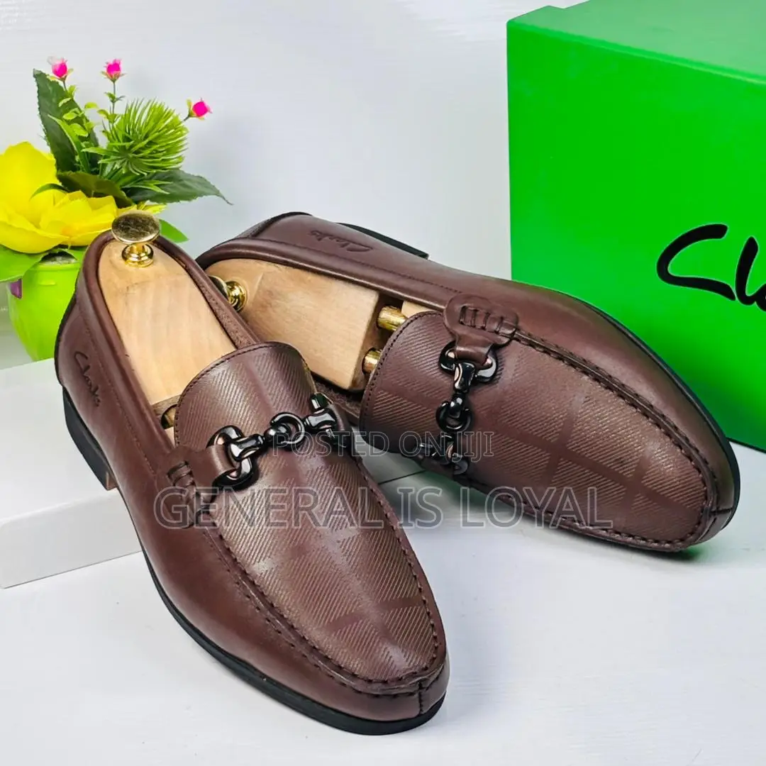 Brown Clarks Loafers With A Metal Buckle And Patterned Leather.